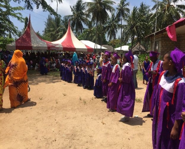 Line of pupils in purple graduation gowns processing past red and white tents