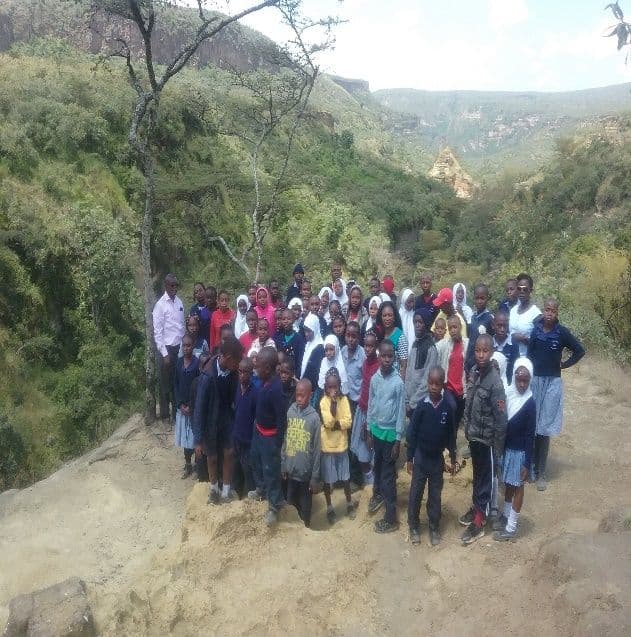 Pupils and teachers posing in a group on rocks above a wooded gorge