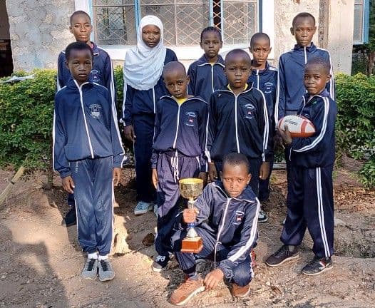 Team of pupils in navy tracksuits posing with a trophy and a rugby ball
