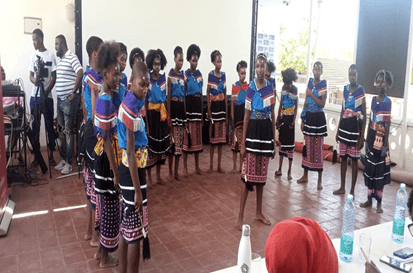 Pupils in colourful traditional costumes standing in a semicircle, performing in a hall