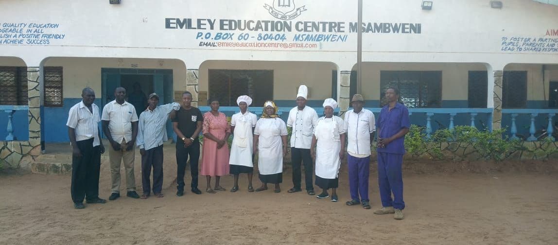 Support staff, including cooks in white uniforms, standing in front of the Emley Education Centre building