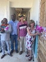 Two visitors and two school staff standing at a classroom doorway, one woman holding a bouquet of pink flowers