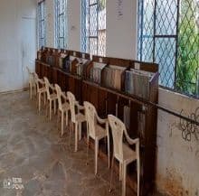 School library with rows of white plastic chairs facing wooden bookshelves along the wall