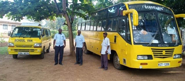 Yellow school van and yellow school bus parked under trees with three men standing beside them