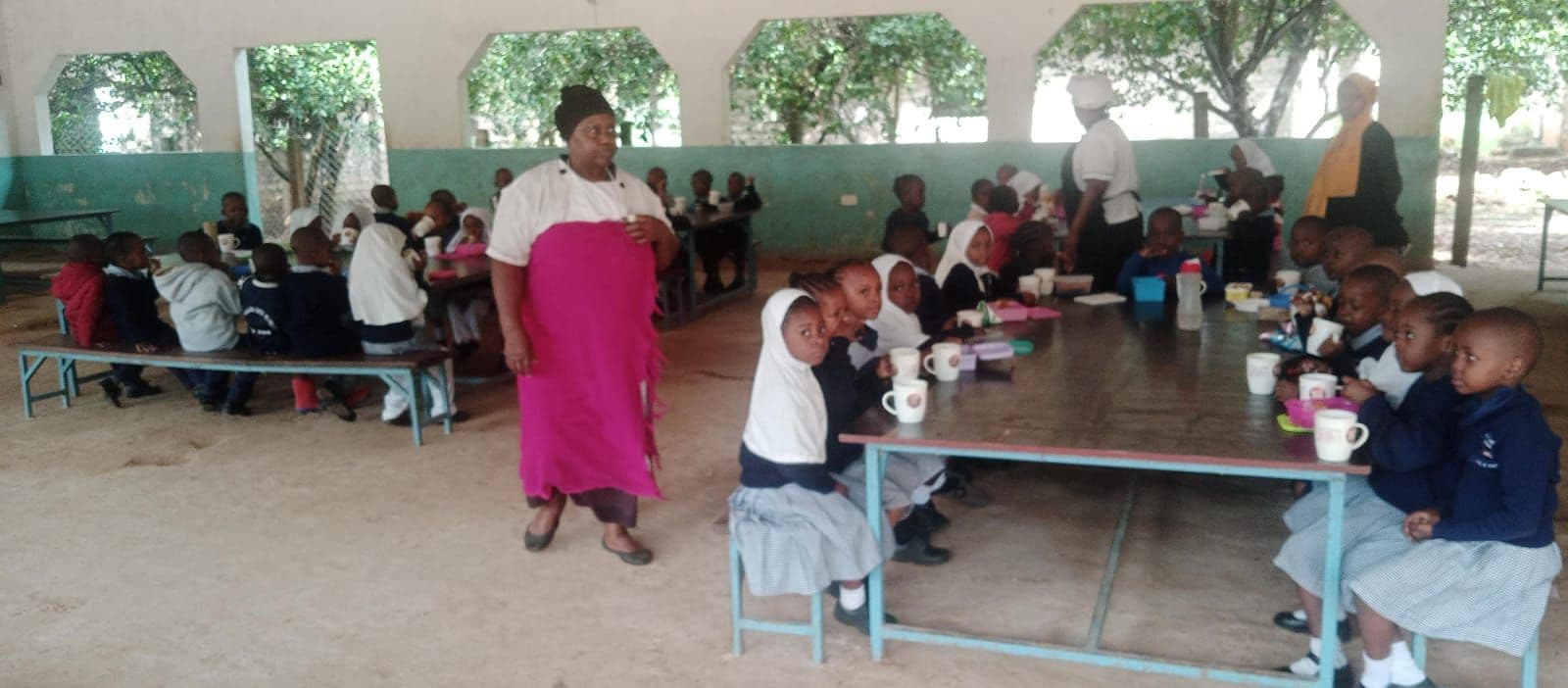 Pupils at long tables having a meal in the open-sided dining hall