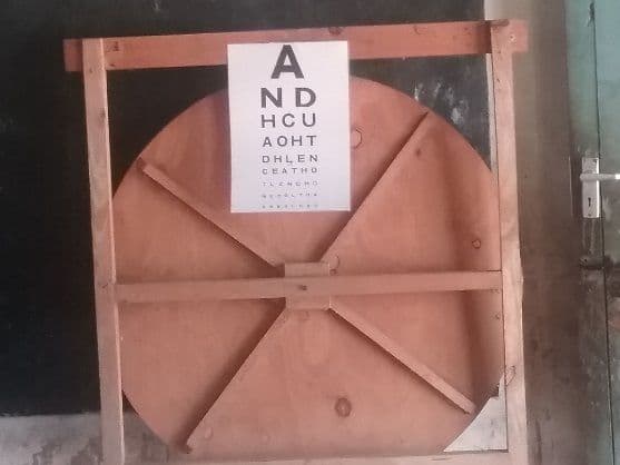 An eye test letter chart pinned to a wooden board against a classroom wall