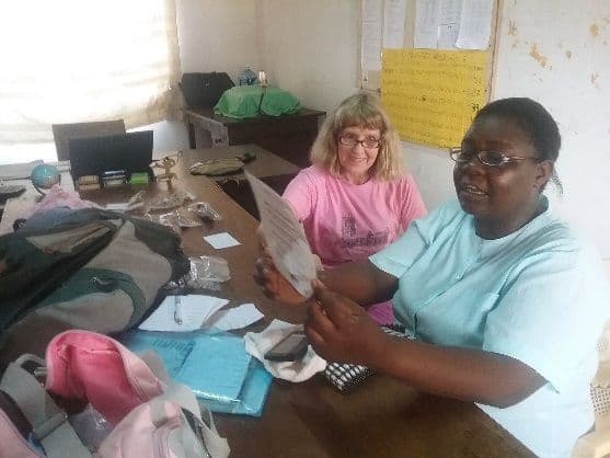 A woman holds up a reading card at a desk of spectacles beside a smiling volunteer