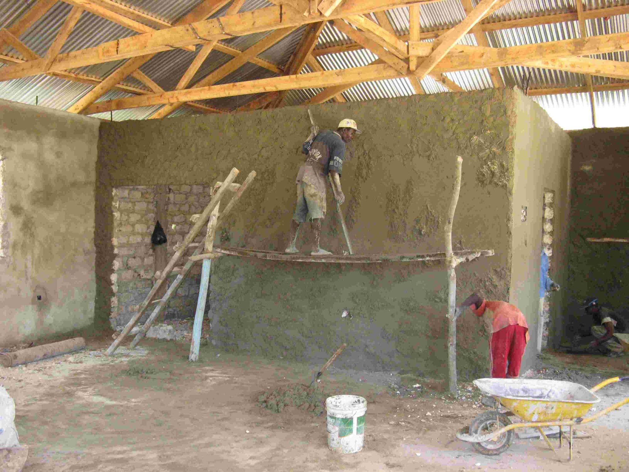 A builder on wooden scaffolding plastering an inside wall of the library