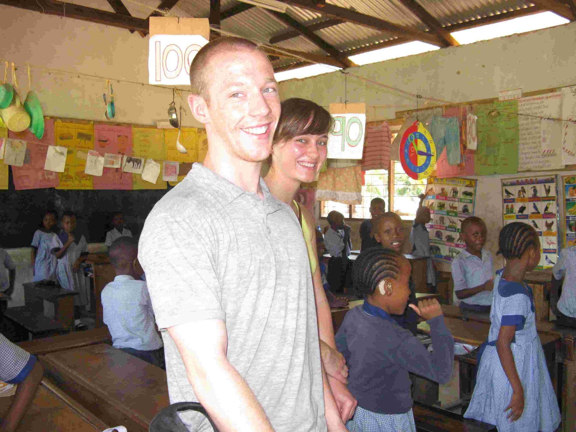 A young couple of visitors smiling in a classroom full of pupils