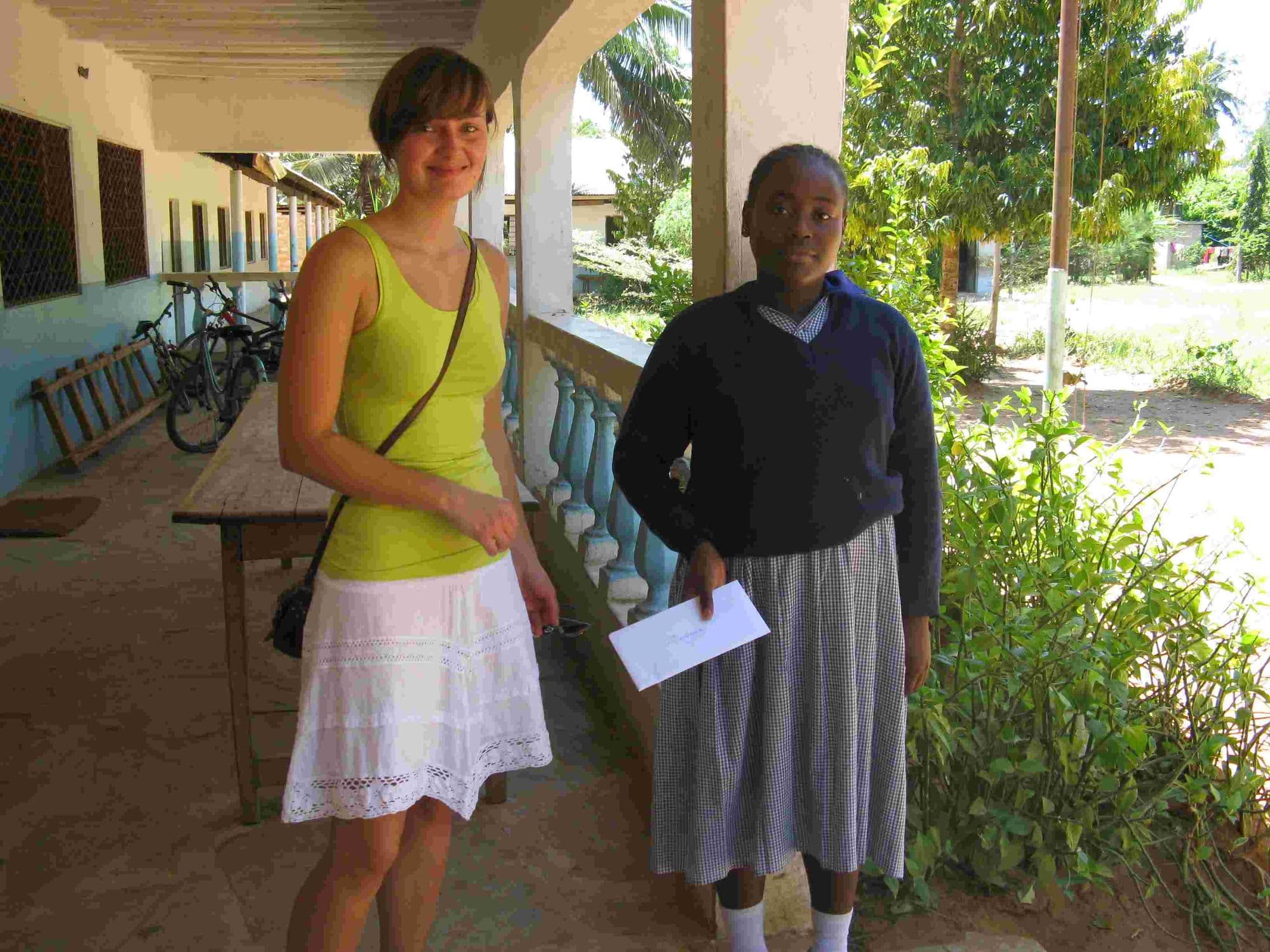 A visitor standing with a schoolgirl on the classroom verandah