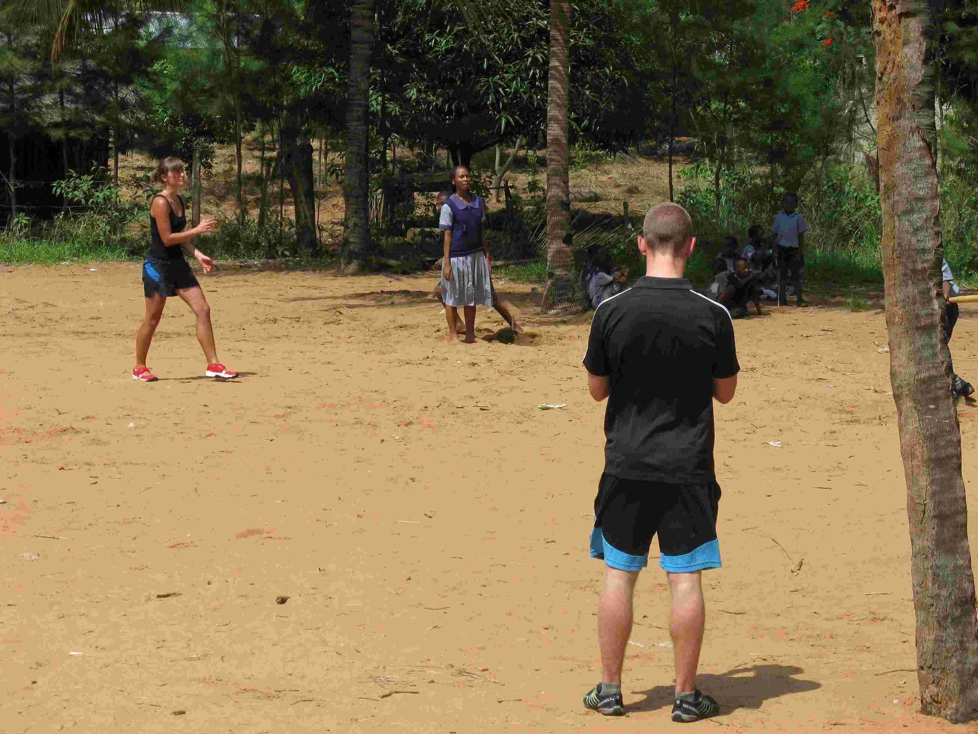 Visitors playing a ball game with pupils on the sandy school field