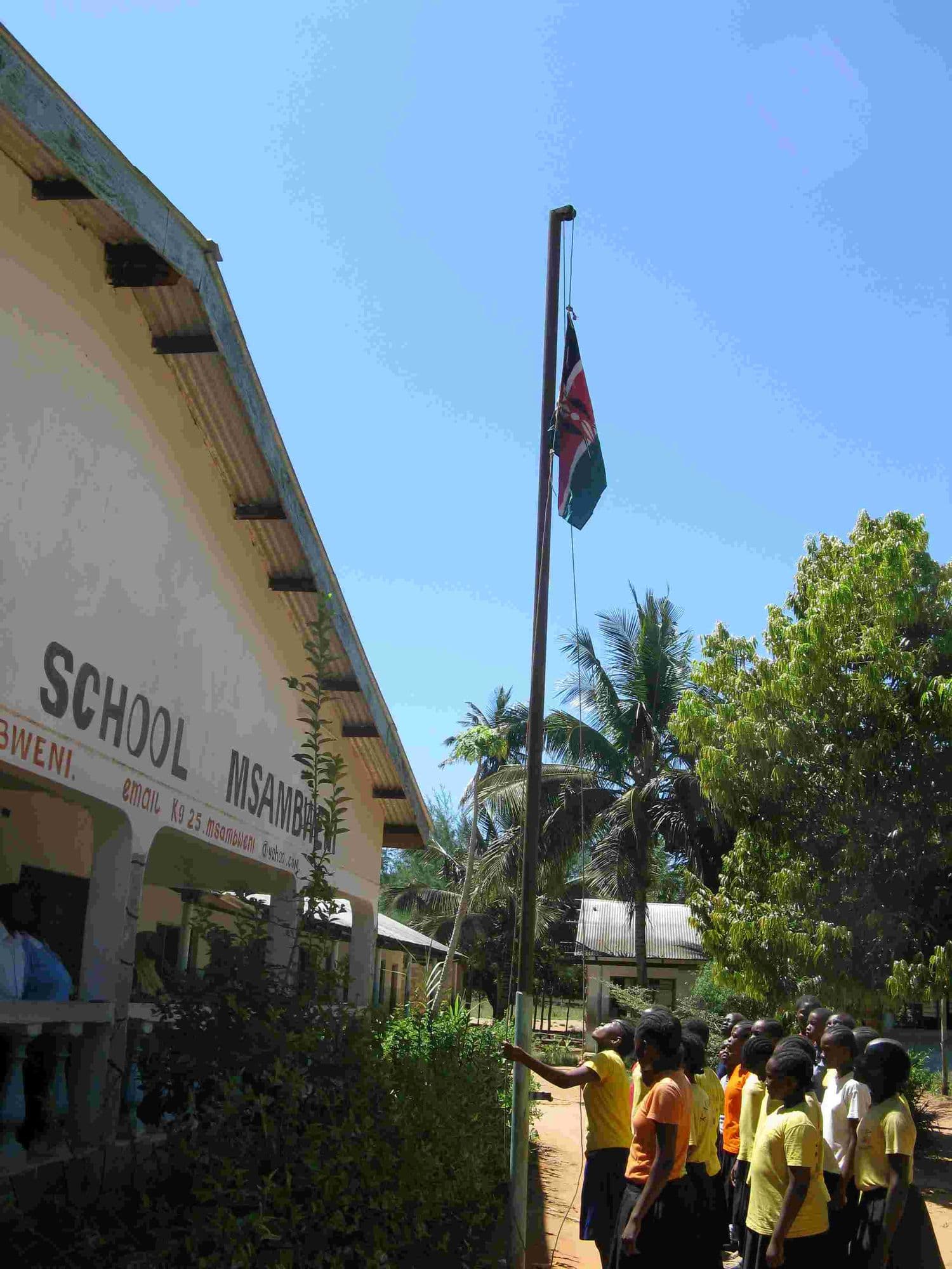 The Kenyan flag raised on a flagpole beside the school building