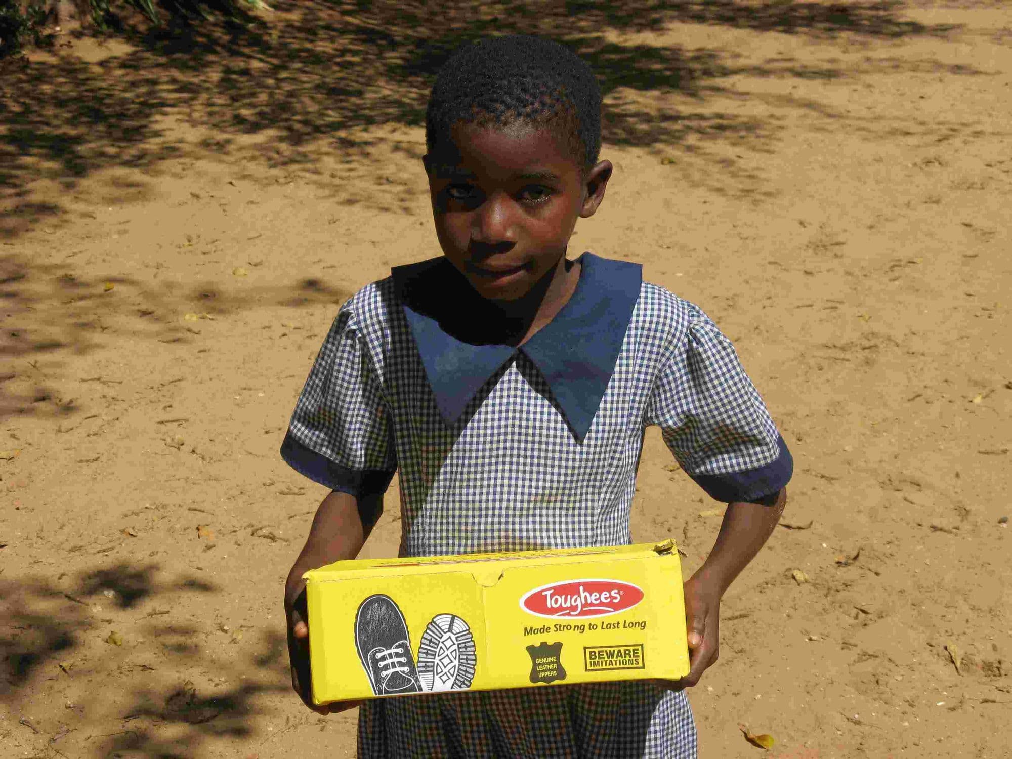 A girl in school uniform holding a new pair of shoes in a box