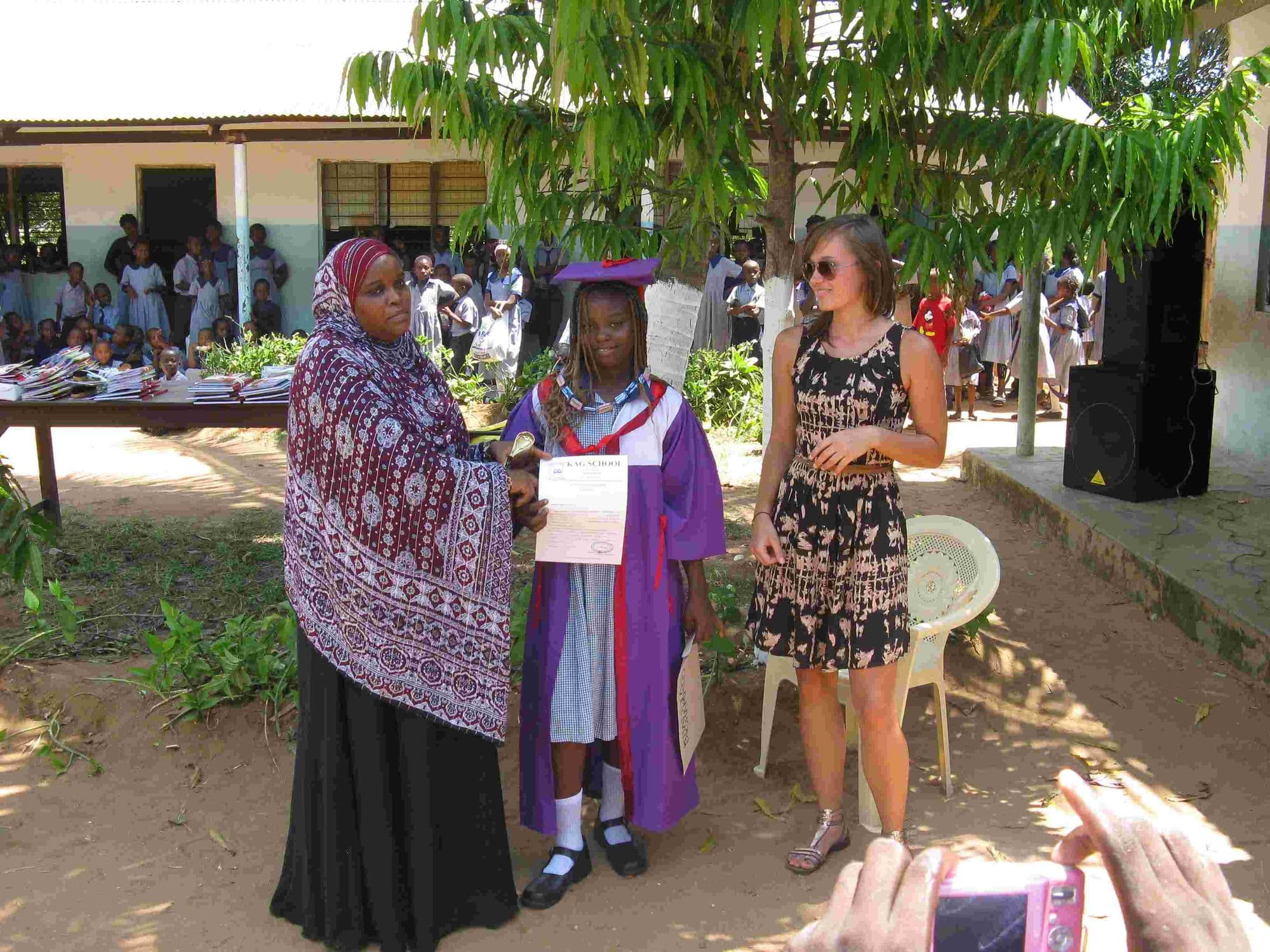 A young graduate holding a certificate between a mother in a headscarf and a visitor