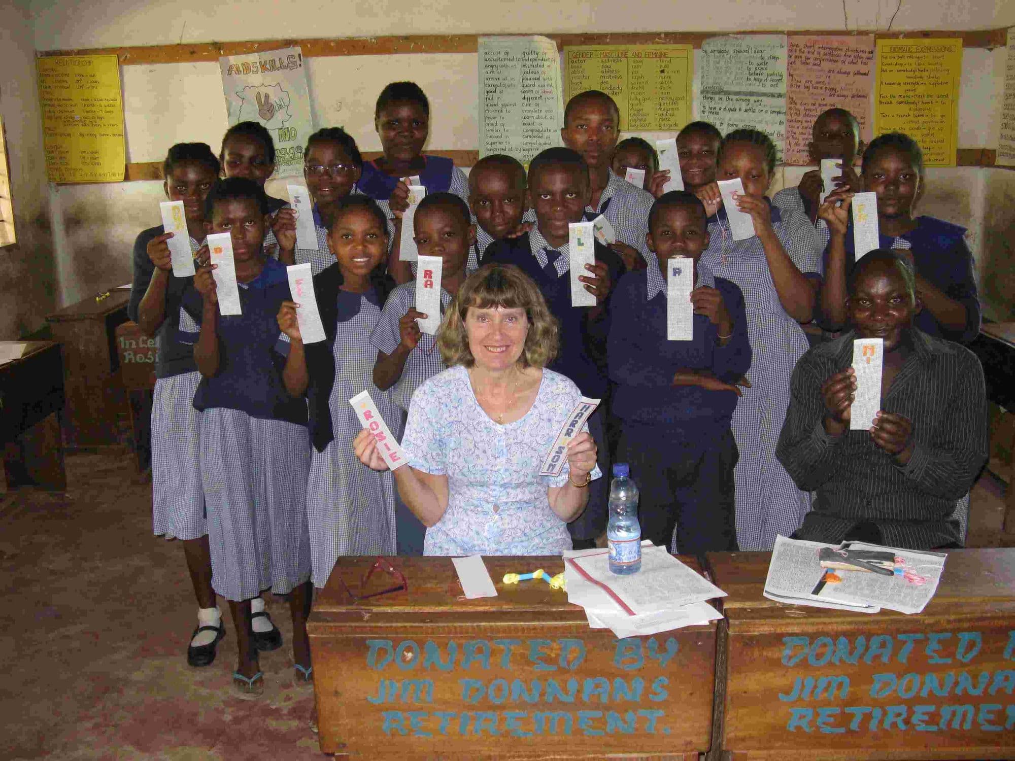 A visitor seated with a class of pupils holding up the sewing they made