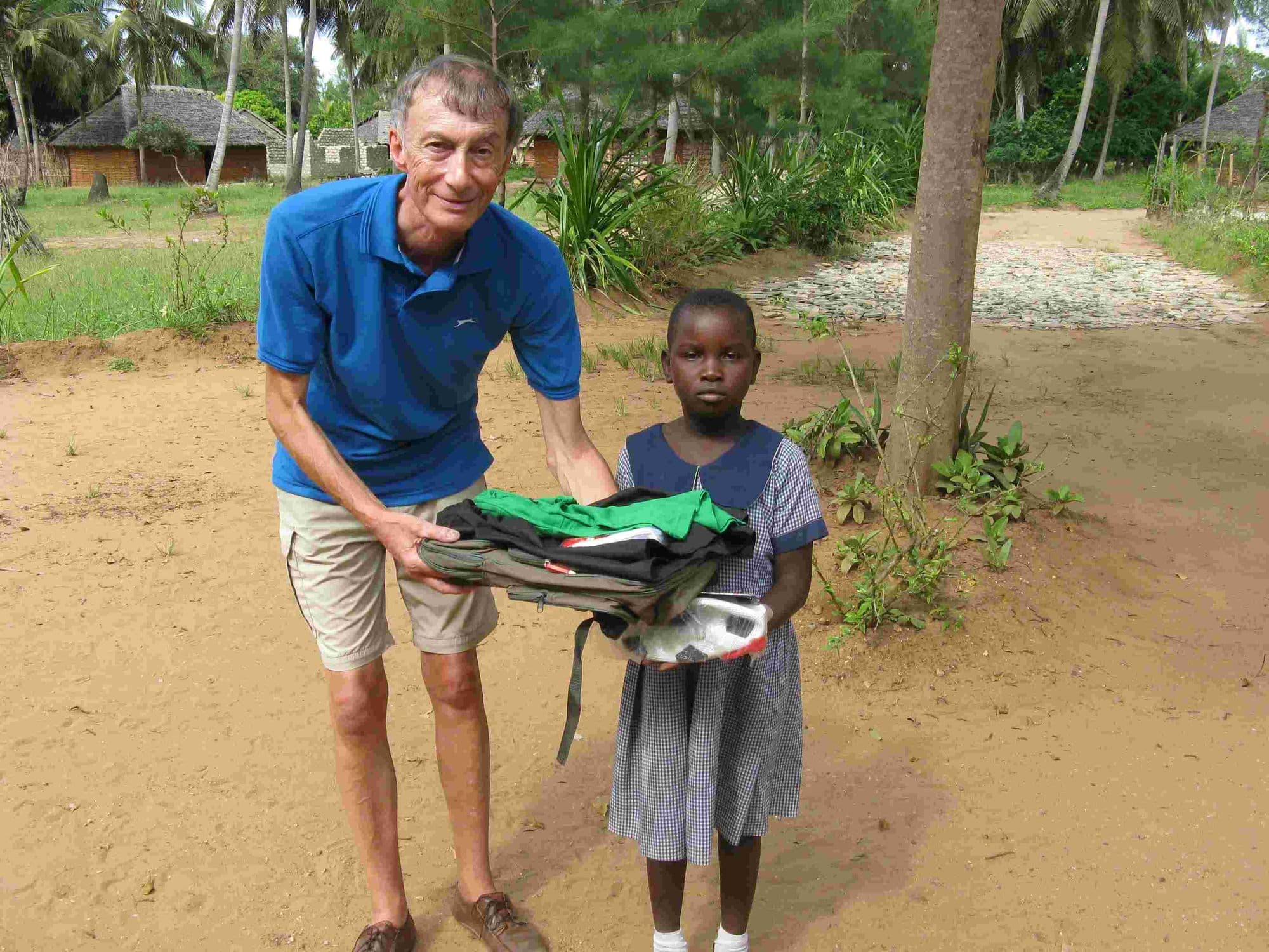 A visitor handing a school bag and uniform to a girl outside
