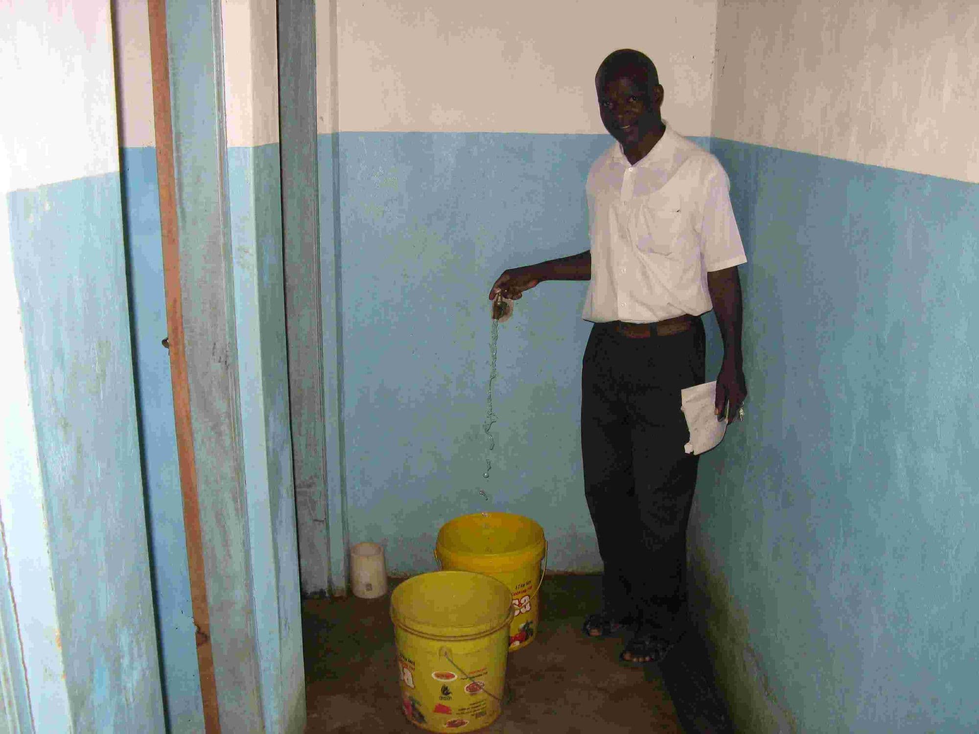 A man pouring water from a newly piped tap into yellow buckets