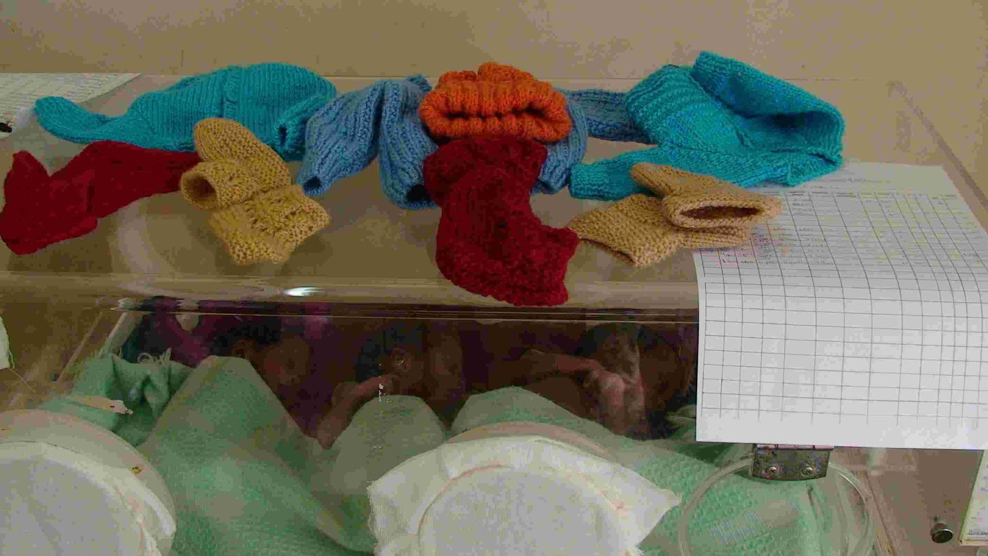 Knitted baby hats and bootees laid on top of a hospital incubator
