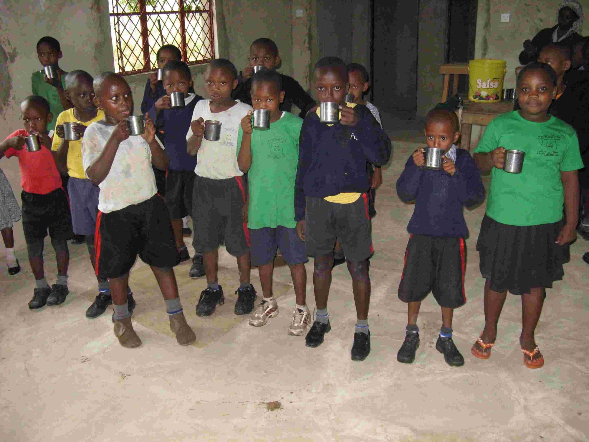 Young pupils standing in a line drinking porridge from metal cups
