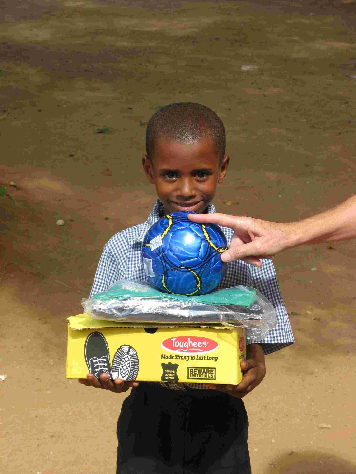 A young boy holding a football and a box of new shoes