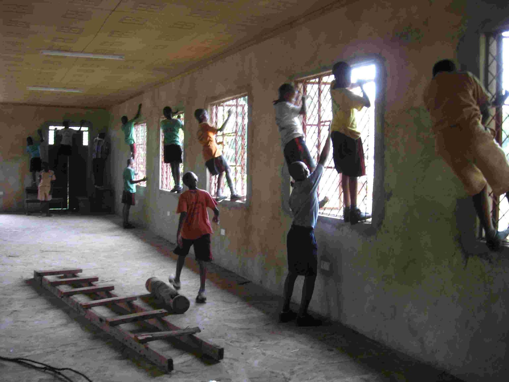Pupils standing on window ledges wiping down the plastered walls of a large room