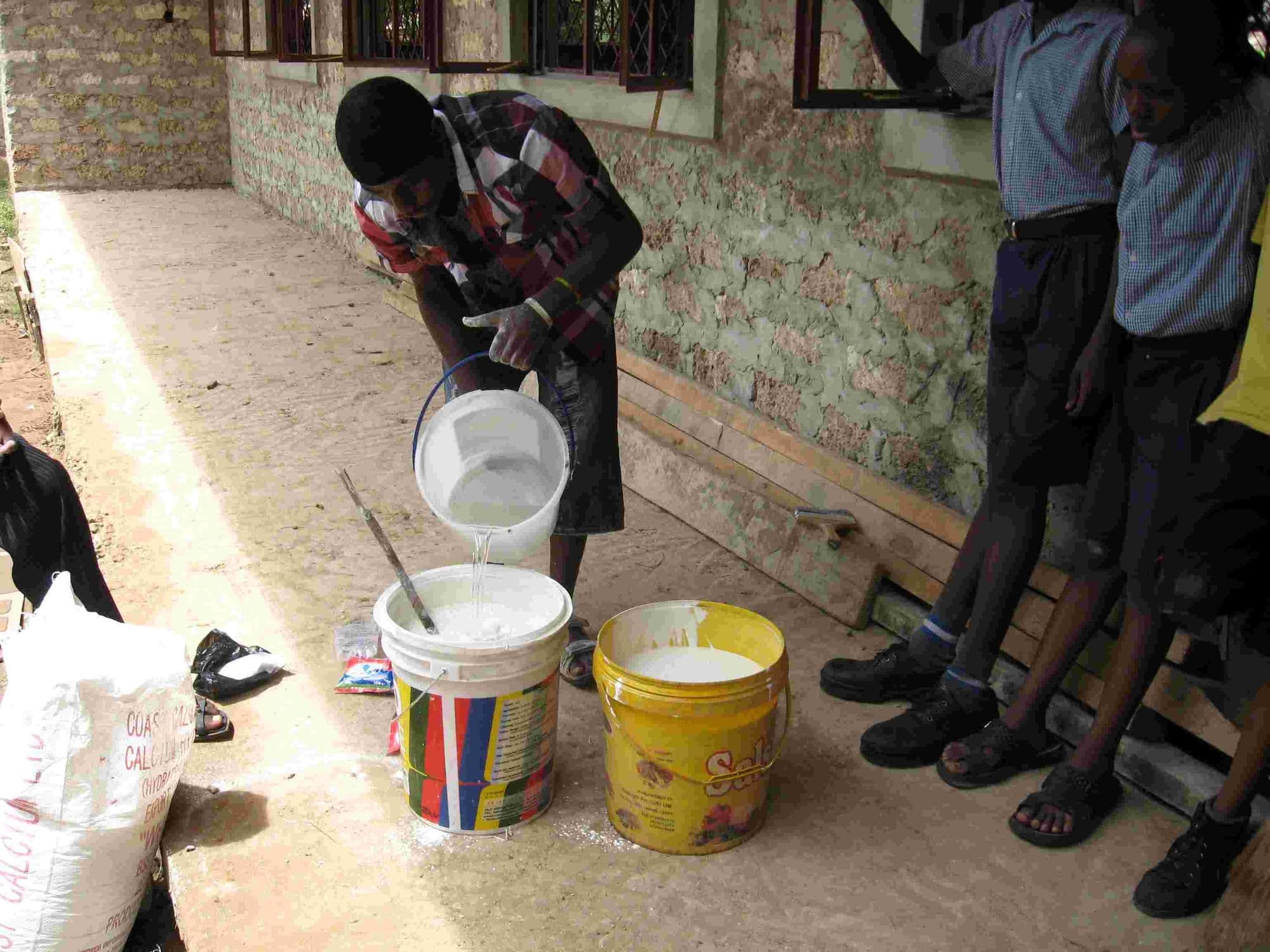 Pupils pouring white paint into buckets ready to paint the walls