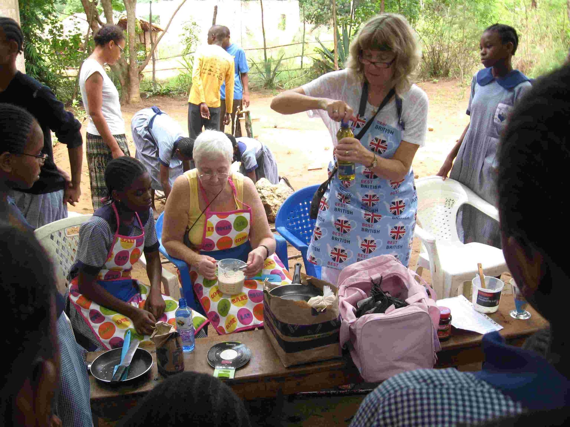 Visitors in aprons cooking with pupils at tables set up outdoors