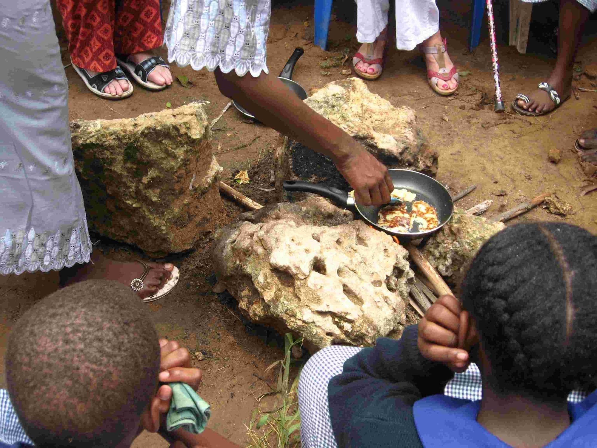 A pan of drop scones cooking on an open fire between stones