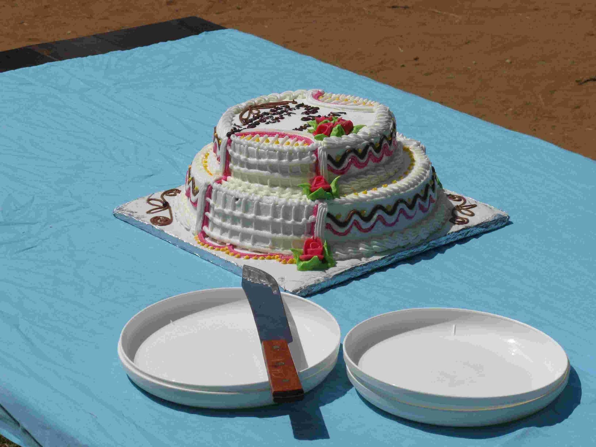 A tiered iced graduation cake on a blue tablecloth with plates and a knife