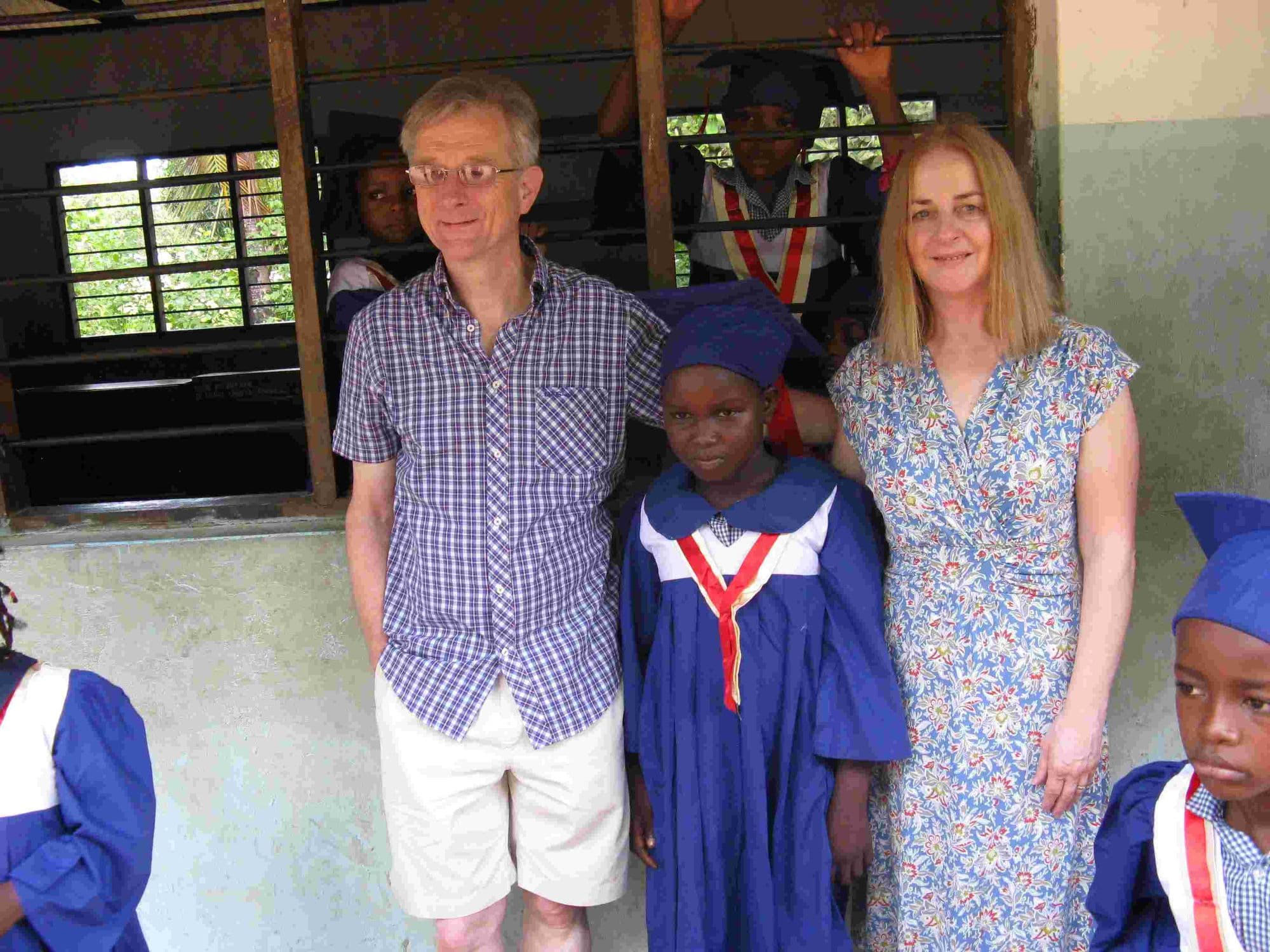 Two visitors standing with a young graduate in a blue gown
