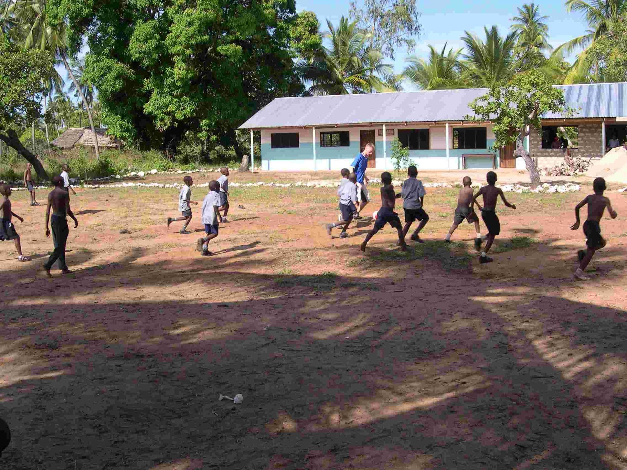 Boys playing football on a sandy field in front of a school block