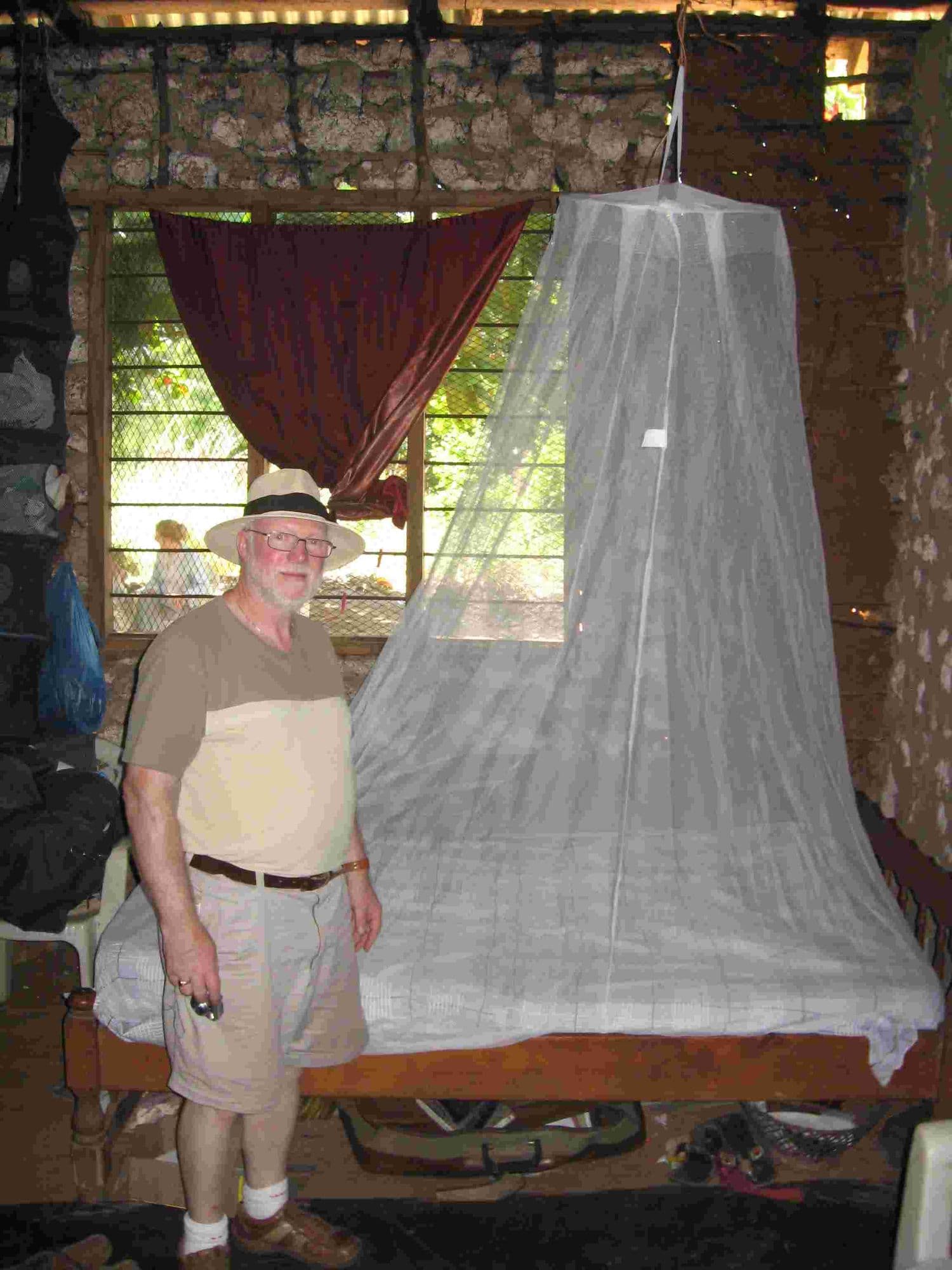 A visitor standing beside a bed with a newly hung mosquito net