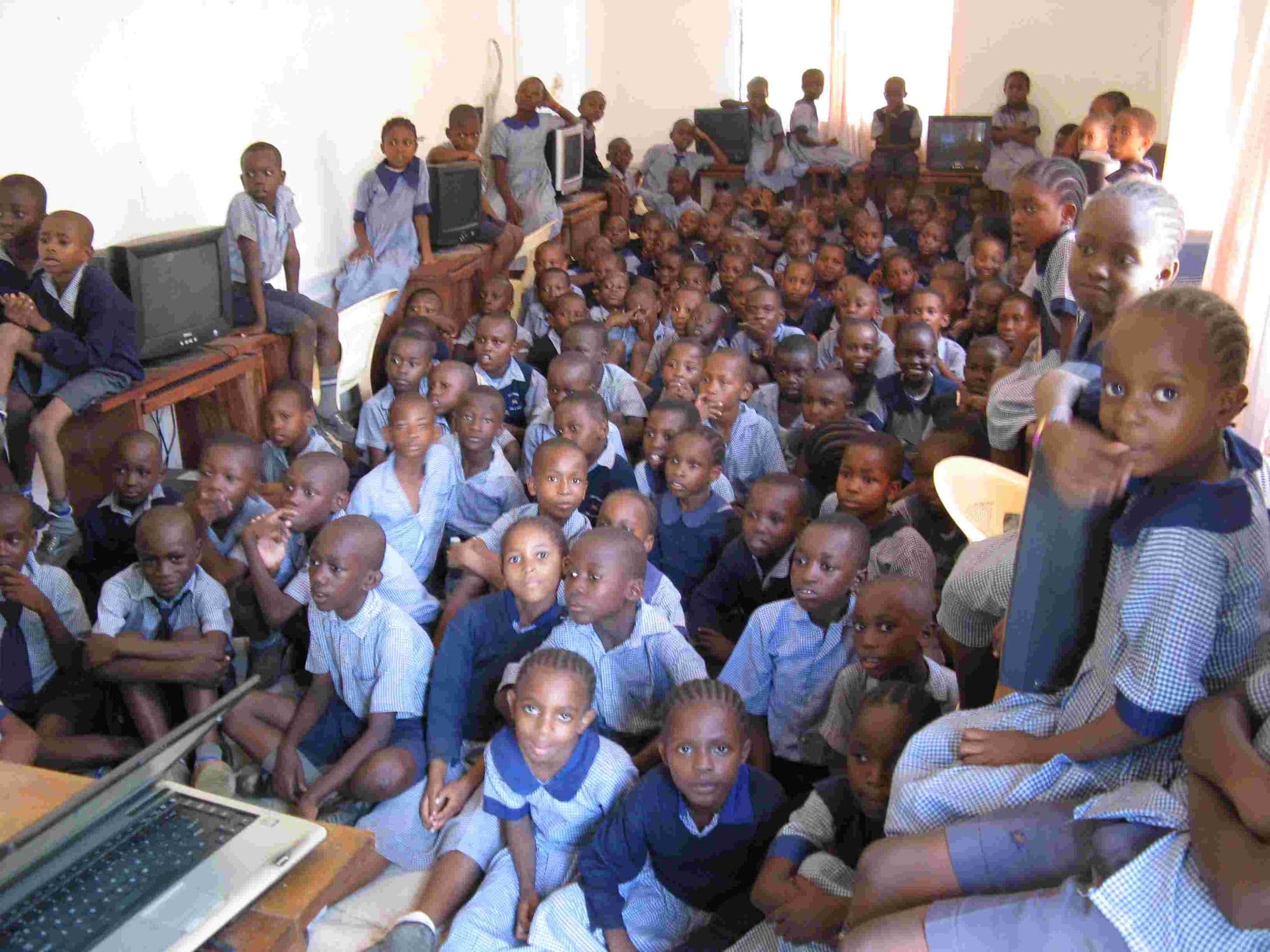 A crowd of pupils sitting on the floor watching a film on a laptop