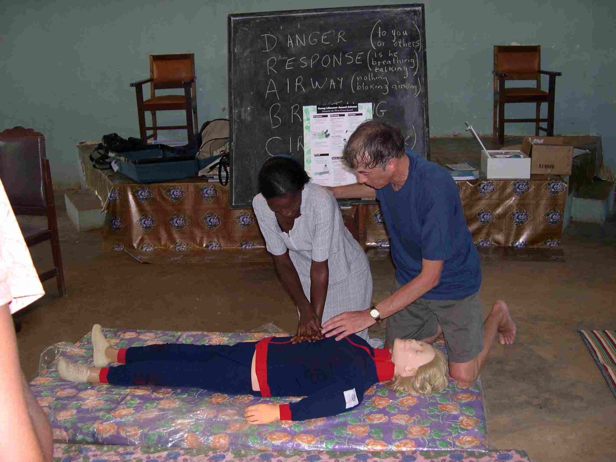 A first aid demonstration of chest compressions on a training dummy in a classroom