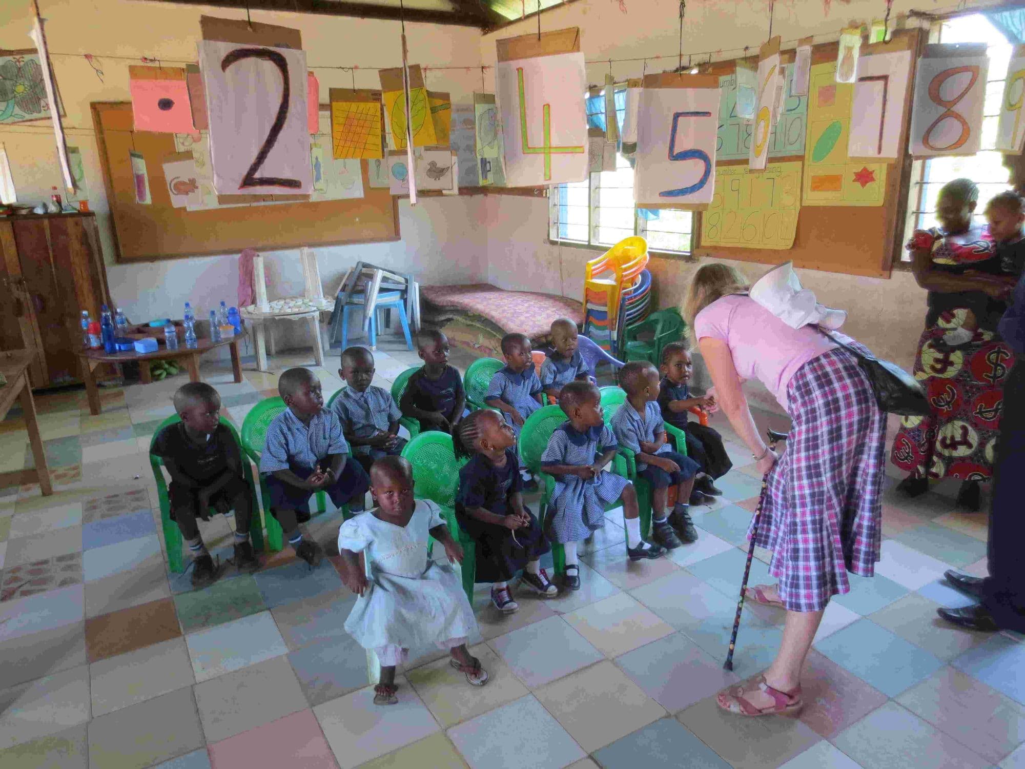 A visitor leading a game with young pupils on chairs in a classroom