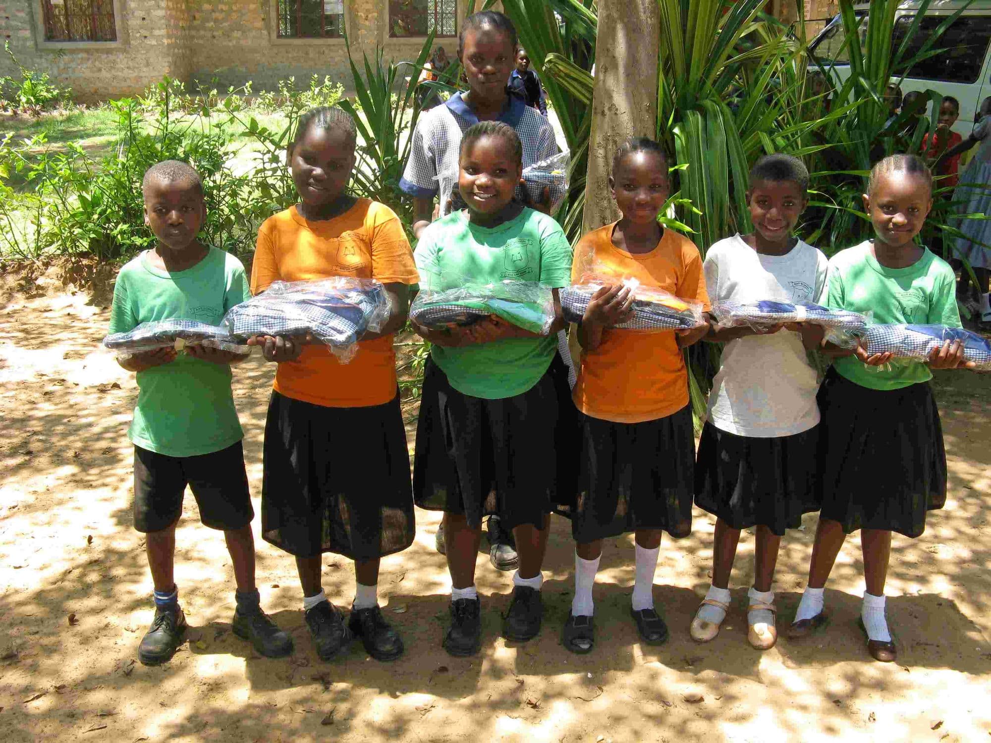 Six pupils holding up new uniforms in plastic packets