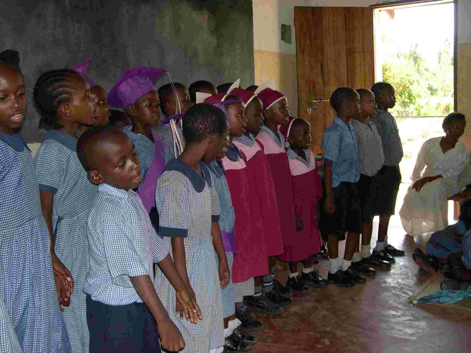 Pupils in uniform standing in rows inside a classroom during a ceremony