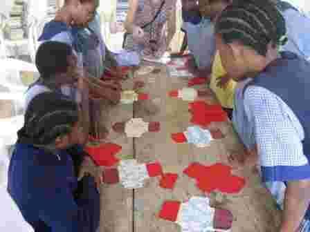 Schoolgirls gathered round a table of cut-out fabric pieces for making sanitary pads