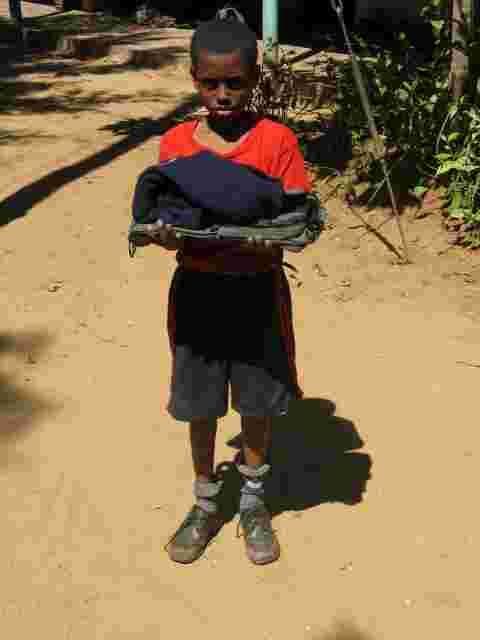 A boy holding a new set of clothes outside his home