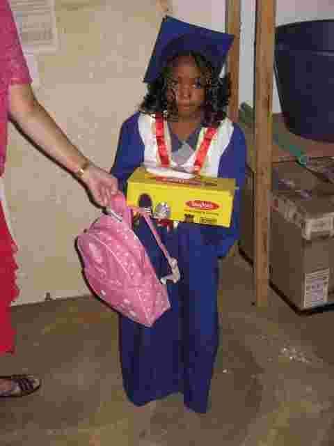 A young graduate in a blue gown receiving a gift box and a pink school bag