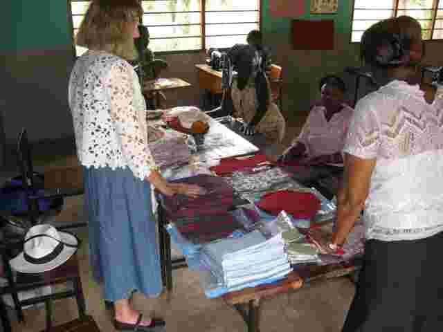 A visitor showing women how to make sanitary wear at a table piled with fabric