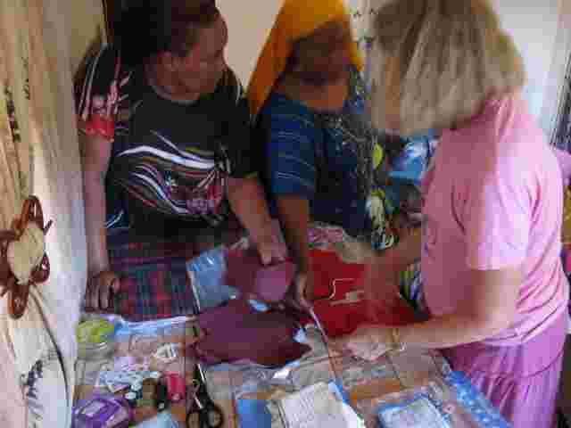 A visitor helping women sort fabric pieces for sanitary kits
