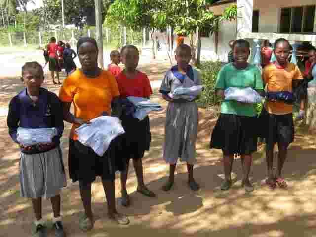 Sponsored pupils holding new uniforms in packets on the school grounds
