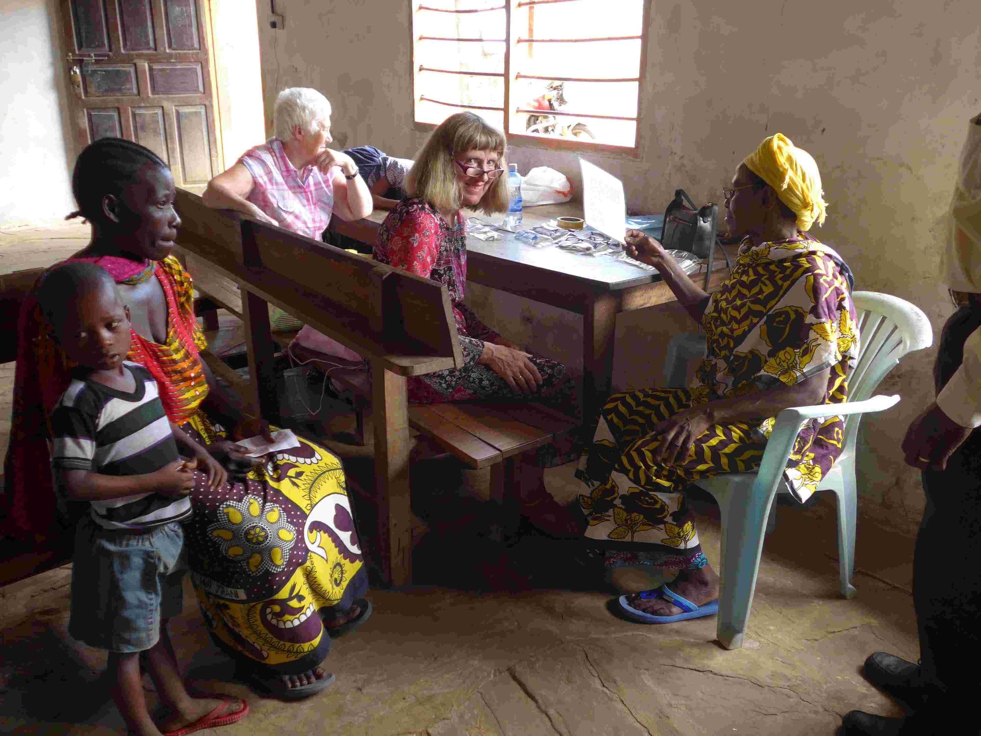 Visitors at a desk recording names and handing out reading glasses to waiting villagers