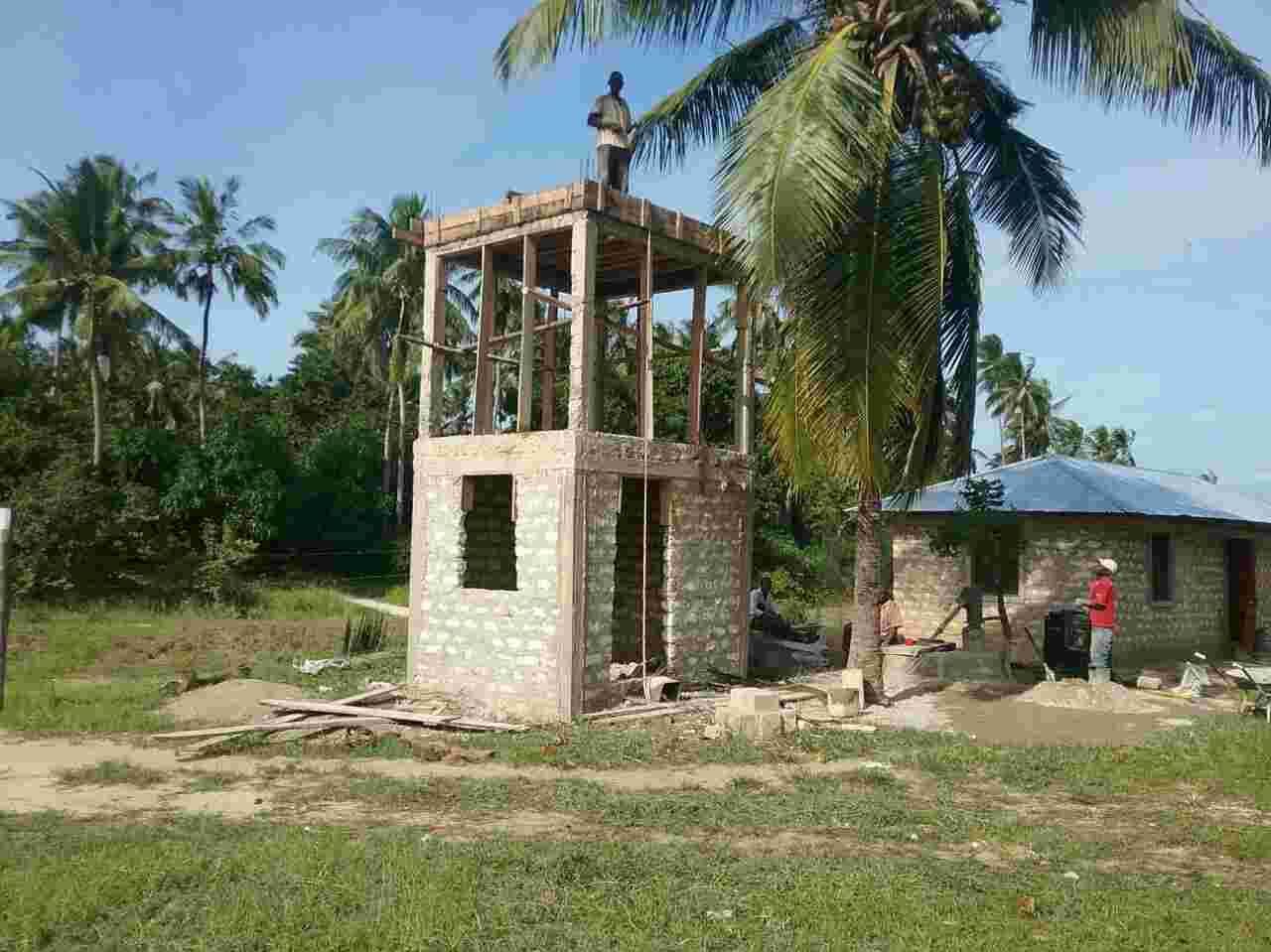 A block water tower under construction at the orphanage with a worker on top
