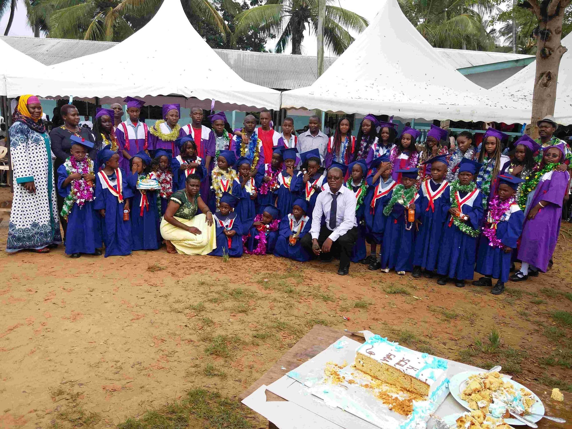 A large group of graduates, teachers and parents posed under marquees with a cake in front