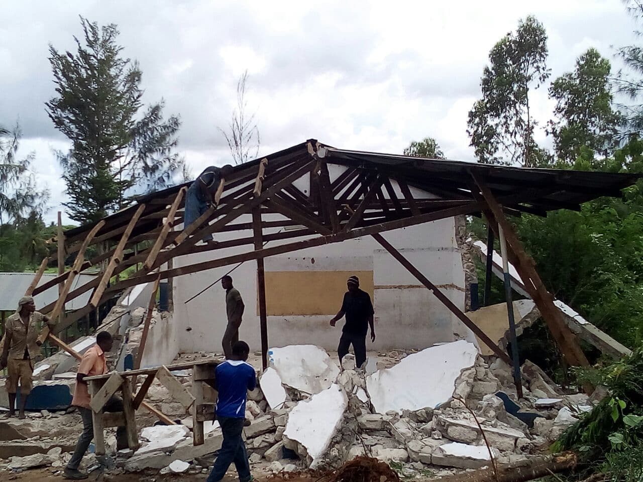 The roof frame of the demolished classroom collapsed among rubble with people salvaging