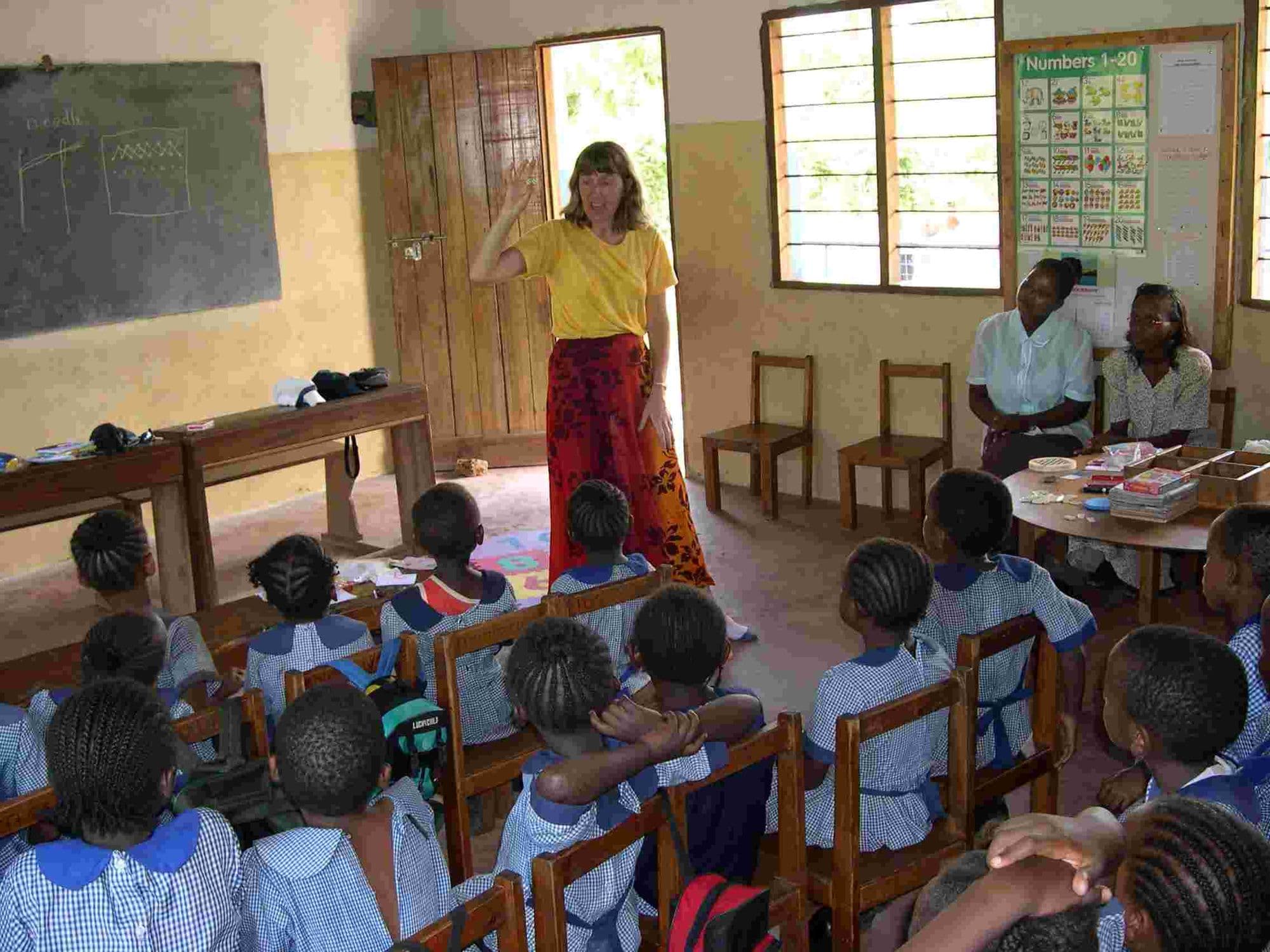 A woman teaching a class of pupils seated at desks in a classroom