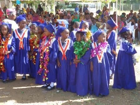 Nursery graduates in blue gowns and tinsel garlands at the graduation ceremony