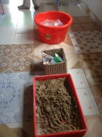 A tray of sand and a basin of water set out as play stations on the classroom floor